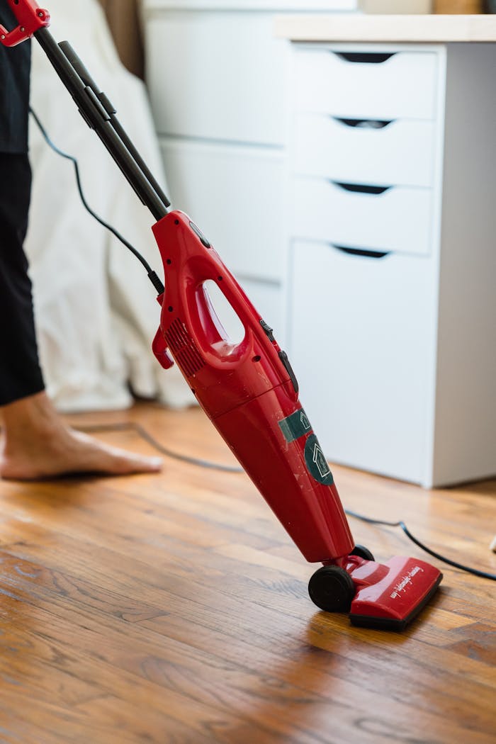 Close-up of a red vacuum cleaner being used on a wooden floor in a domestic setting.